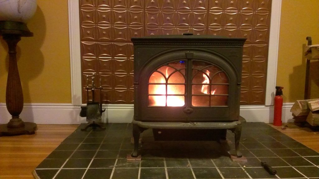 A cast iron wood stove glowing in front of a pressed copper panel