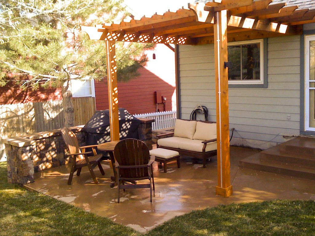 A backyard patio under a timber pergola with outdoor sofas and a dining set