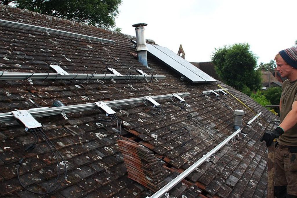 A roofer fitting new rails across a tiled roof